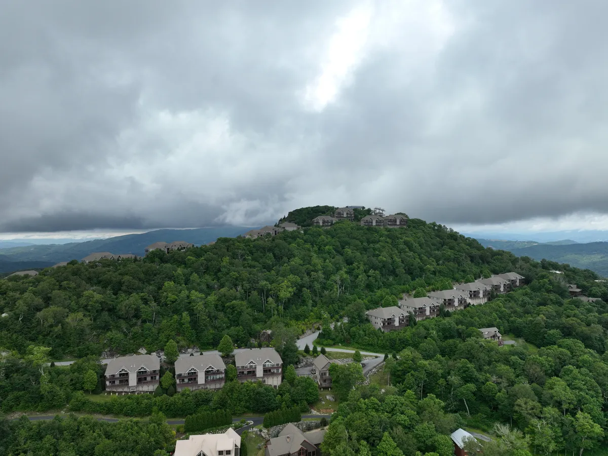 A wide shot featuring residential buildings nestled amid lush greenery with majestic mountains in the background. The peaceful scene evokes the sense of retreat, connection to nature, and easy access to outdoor activities.