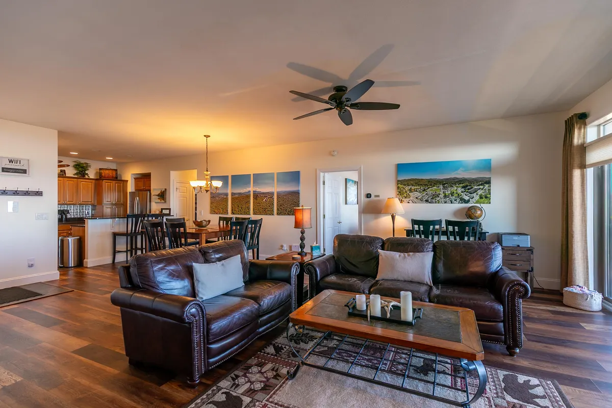 An open-concept space displaying leather sofas, a spacious dining table large enough for group meals or board games, and a kitchen counter. The area is decorated with landscape artwork, adding to the inviting, homey atmosphere ideal for gatherings.