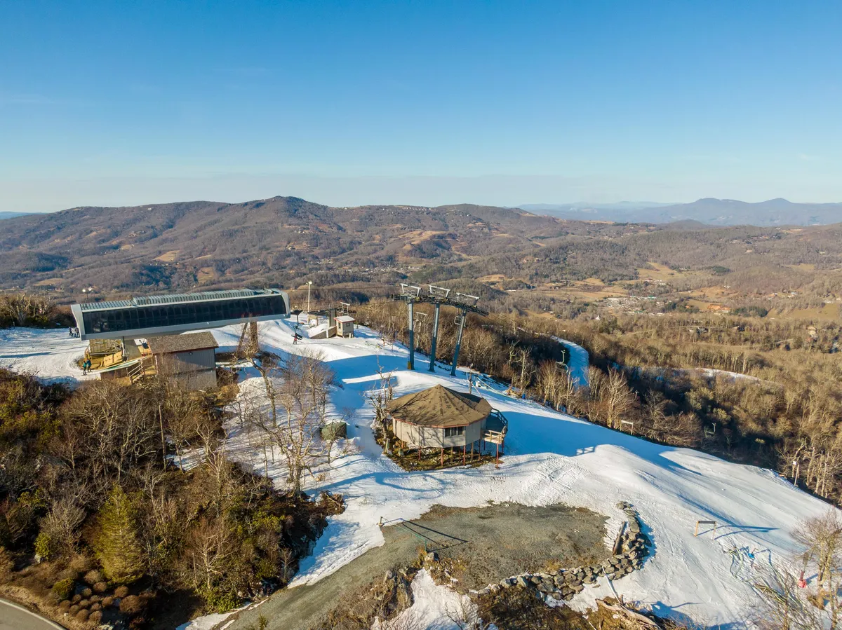 A dynamic exterior scene featuring the ski lift just outside a mountain lodge, with snow-covered slopes and panoramic mountain views in the background. Guests are skiing and snowboarding, capturing the excitement and direct access to winter activities right from the property.