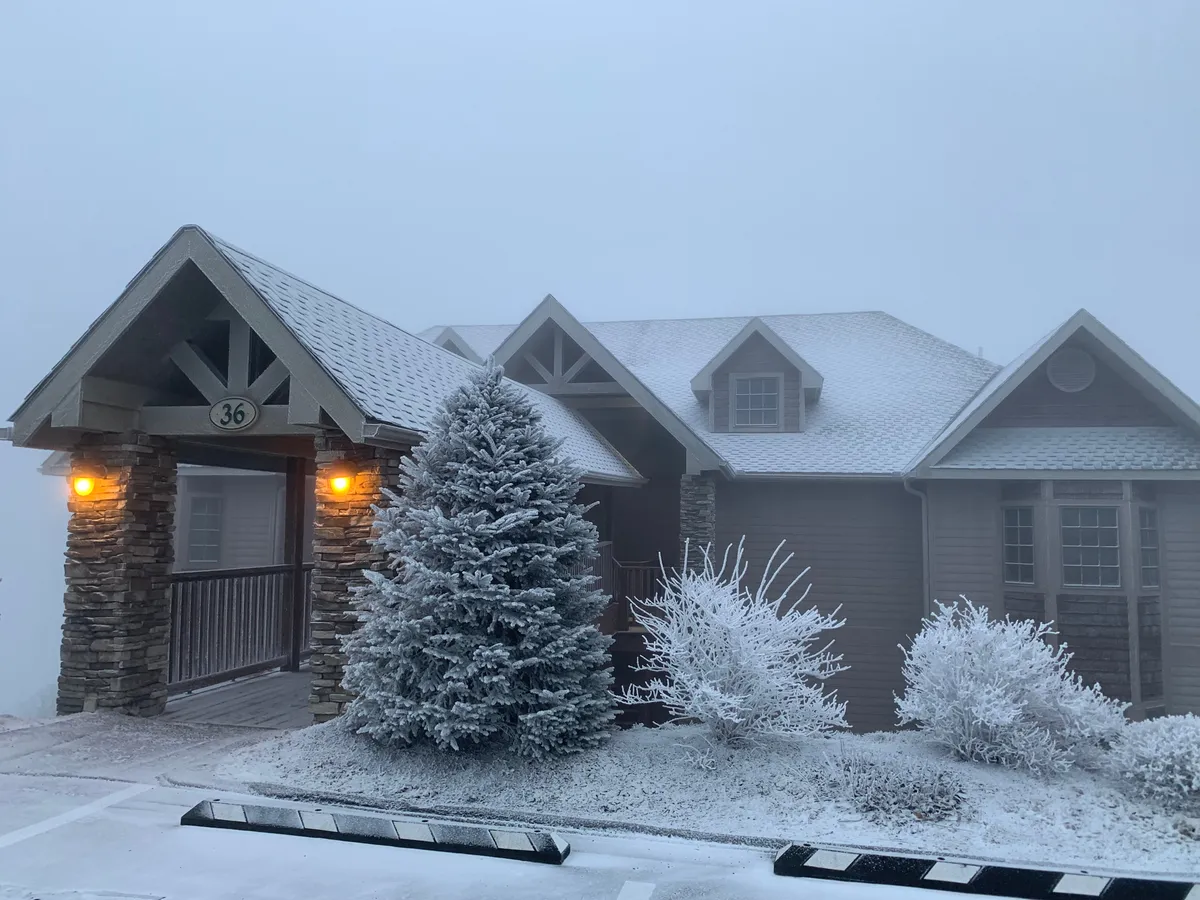 This image shows a welcoming stone entryway framed by snow-covered trees and frosted shrubs. Warm porch lights illuminate the entry, evoking a sense of comfort and luxury in a winter setting. The entry is inviting and clearly marks the transition from the privacy of the condo to the adventure outside.