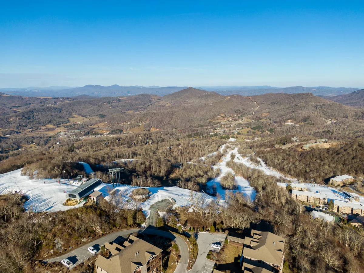 Snow-covered slopes and a ski lift stretch toward distant mountains, with nearby residential buildings nestled among wooded areas. The scene suggests immediate access to winter activities and resort amenities.
