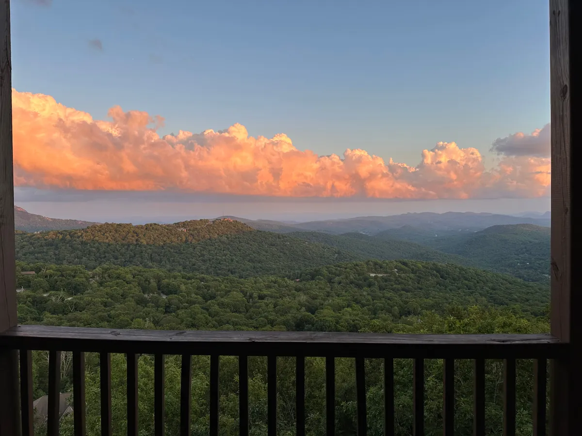 A breathtaking view of a mountainous landscape under a sky filled with colorful clouds, surrounded by lush greenery. The image conveys tranquility and the restorative power of nature, with the vantage point suggesting a perfect spot for a sunrise coffee or evening wind-down.