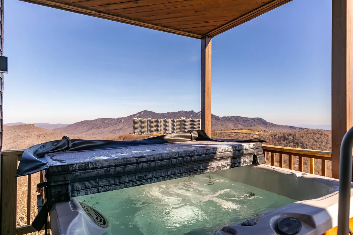 The photo features a hot tub set on a deck with sweeping views of the mountains and sky, ideal for unwinding while immersed in nature. The soft light suggests sunset or early morning tranquility, inviting moments of pure relaxation.