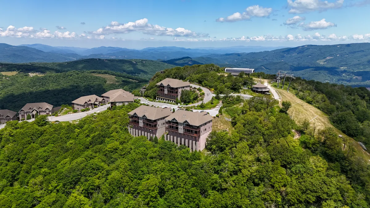 A panoramic view of a mountainous landscape at sunrise, with luxurious cabins nestled along a winding road. The scene suggests opportunities for scenic drives, hiking, and outdoor exploration in a serene setting.