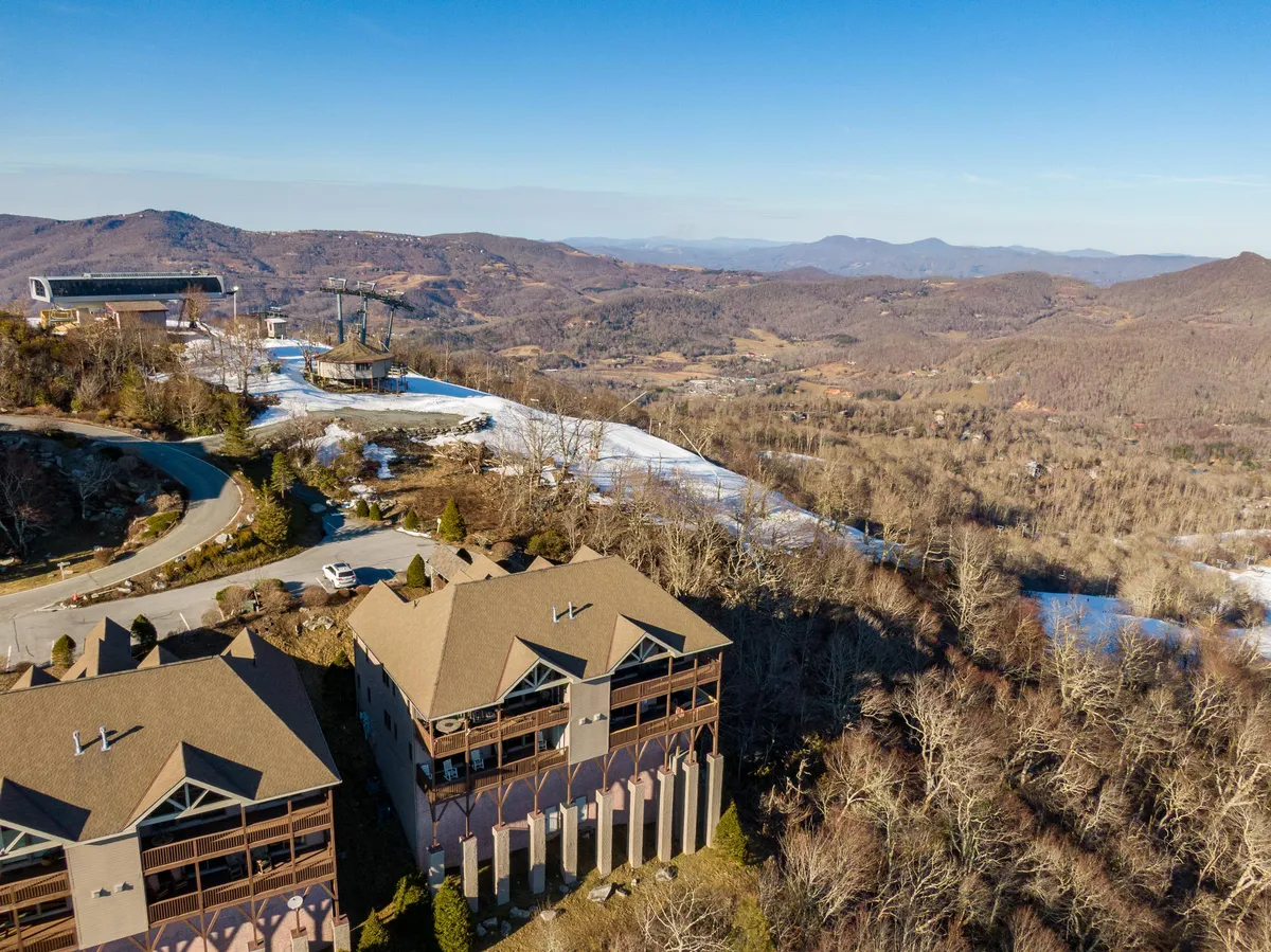 A dynamic exterior view featuring a modern resort building set against a mountain backdrop, with a ski lift visible—indicating year-round activity. The scene merges architectural appeal with natural surroundings and hints at trail access and sunset views.