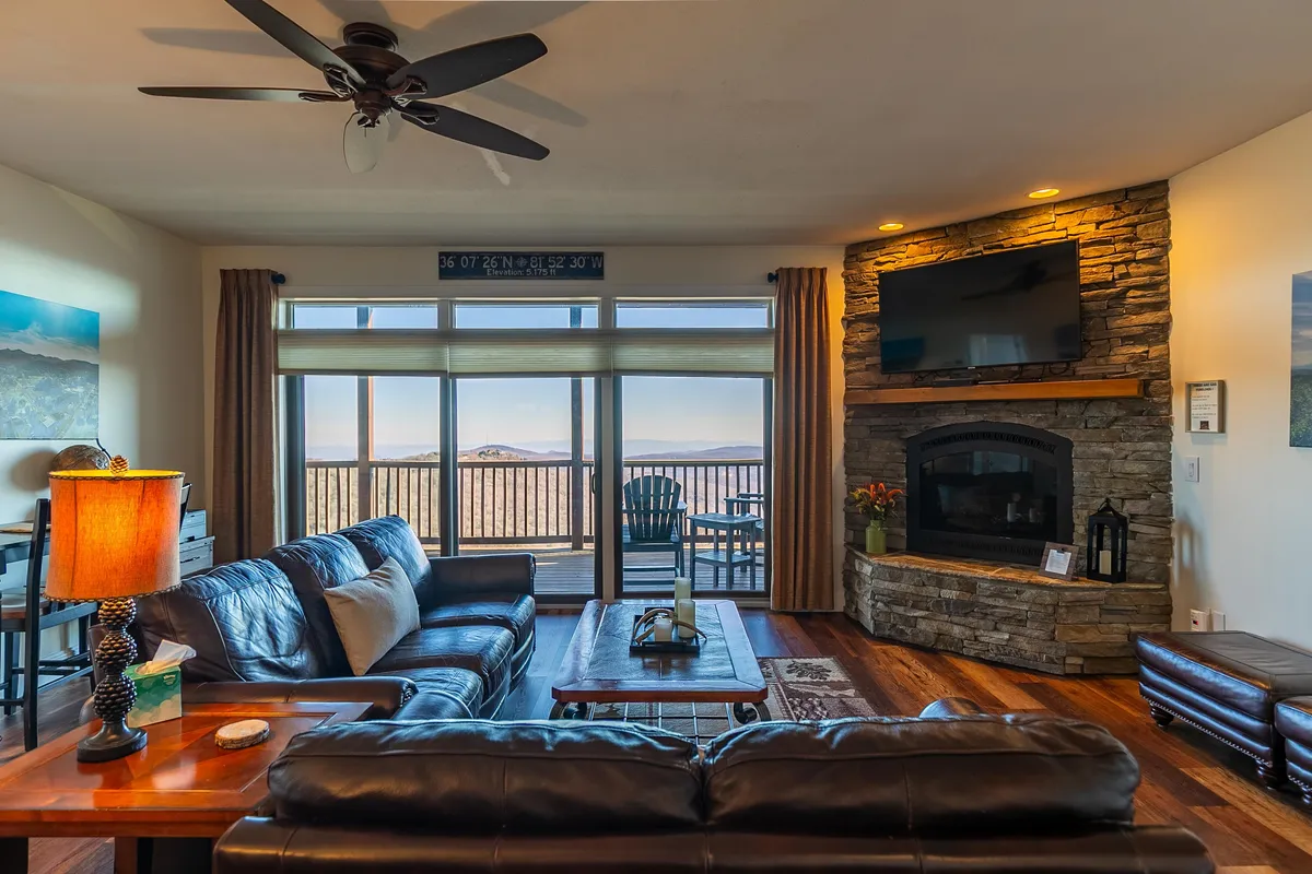 A cozy interior space featuring a leather sofa positioned near a stone fireplace, with large windows offering a view of the outdoors. Warm ambient lighting and inviting decor set the mood for intimate evenings inside, while still maintaining a connection with the surrounding natural beauty.