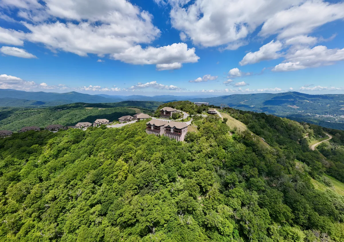 An expansive vista of lush green mountains under a vast sky, dotted with scattered buildings and enveloped in tranquil morning light. The image hints at wildlife observation, hiking, and photography opportunities in the area.
