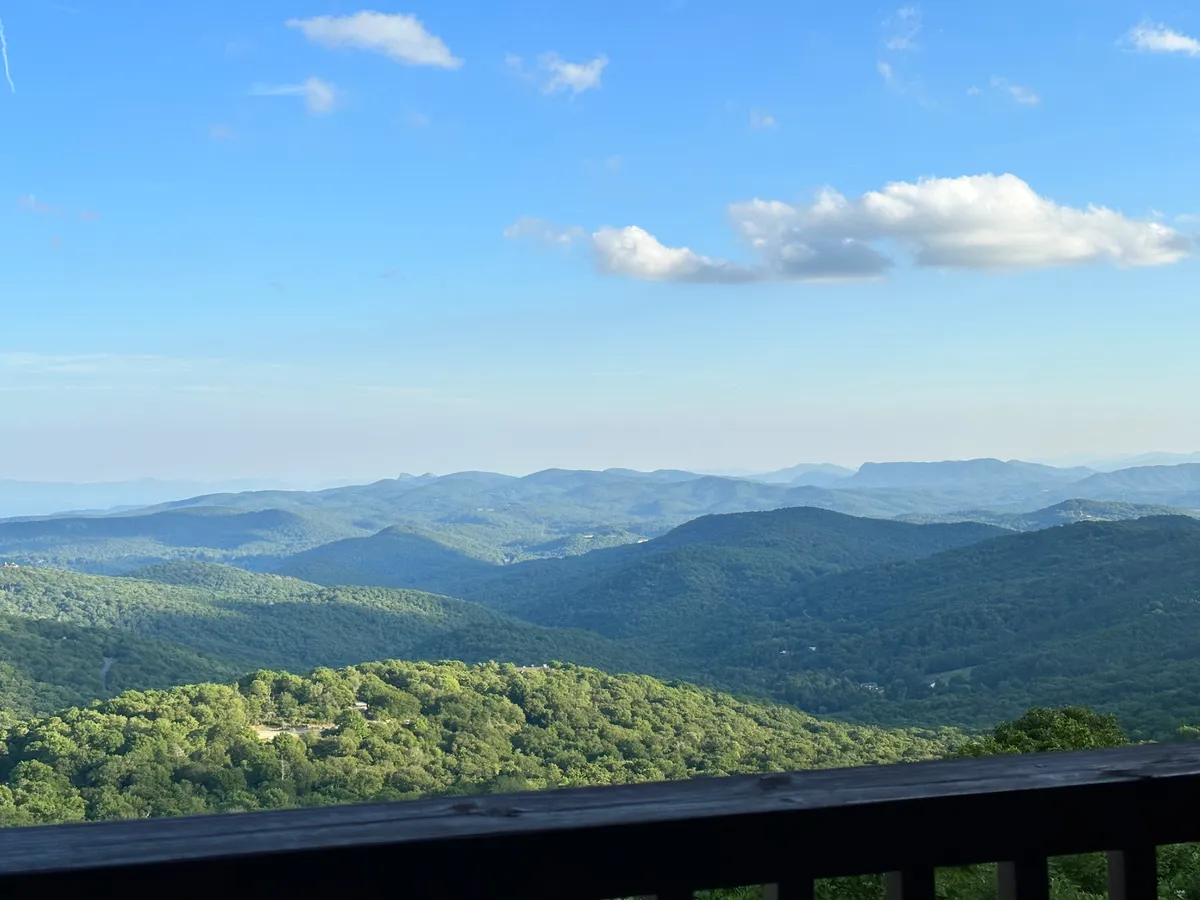 A sweeping view of mountain ranges and verdant green valleys beneath a sky dotted with clouds. The composition is expansive, hinting at possibilities for hiking, contemplation, or simply soaking in the scenery between work sessions.