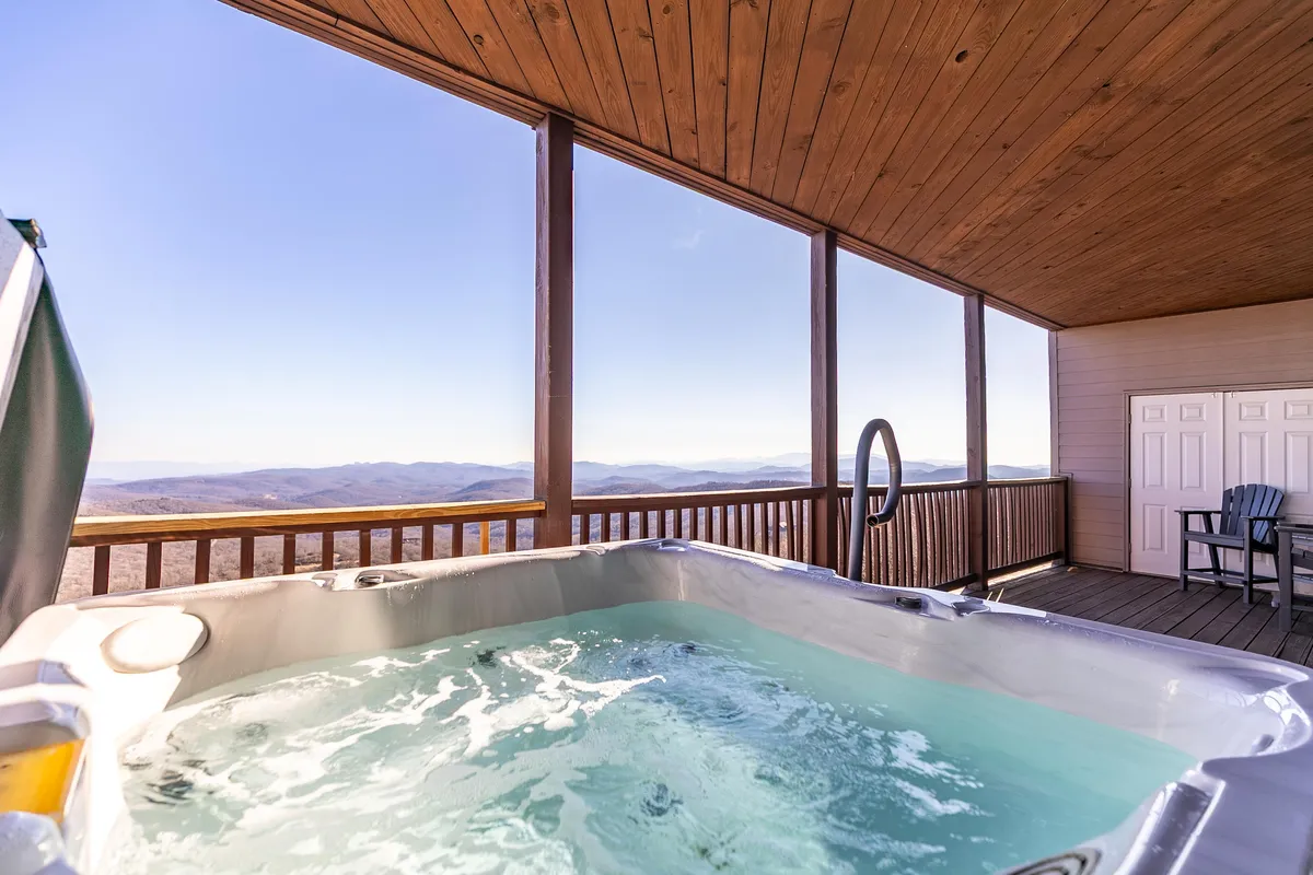 This image captures an inviting outdoor hot tub set on a wooden deck, overlooking rolling mountain scenery. The warm, bubbling water contrasts with the crisp mountain air, while the expansive views hint at a peaceful escape after a day of adventure.